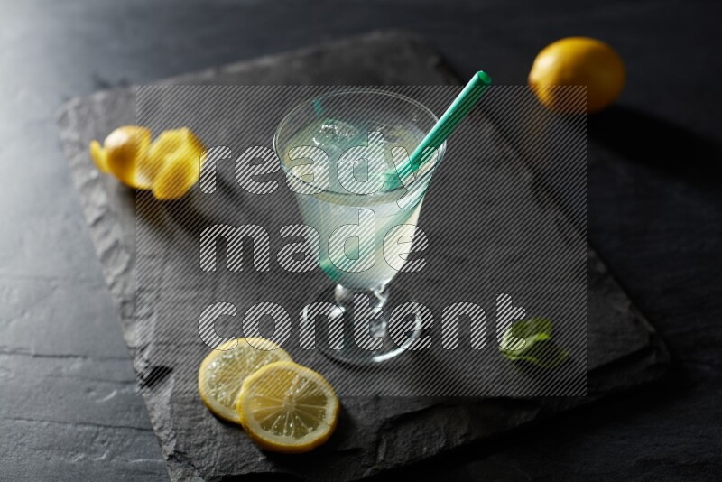 A glass of lemon juice with a straw on black background