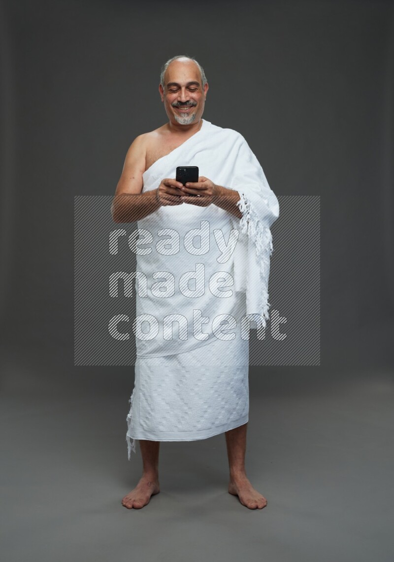A man wearing Ehram Standing texting on phone on gray background