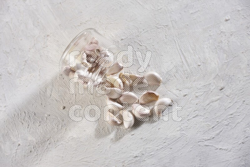 A glass jar full of garlic cloves flipped and the cloves came out on a textured white flooring