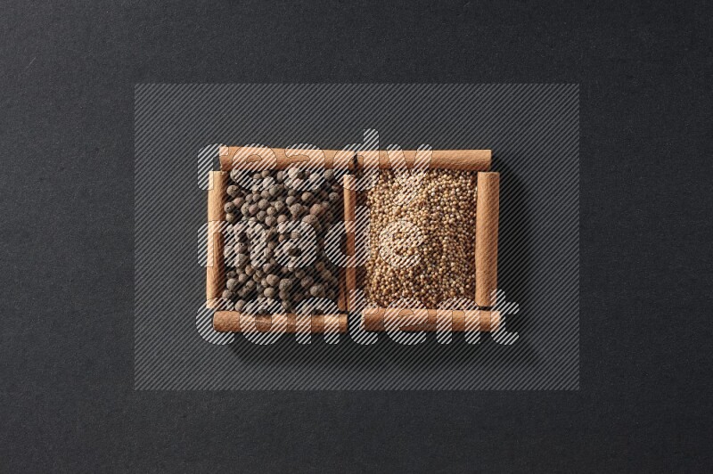 مربعان من أعواد القرفة ممتلئان بحبوب الخردل وحبوب بهار الفلفل الحلو علي خلفية سوداء