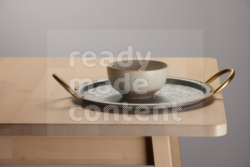 multicolored bowl placed on a rounded stainless steel tray with golden handels on the edge of wooden table
