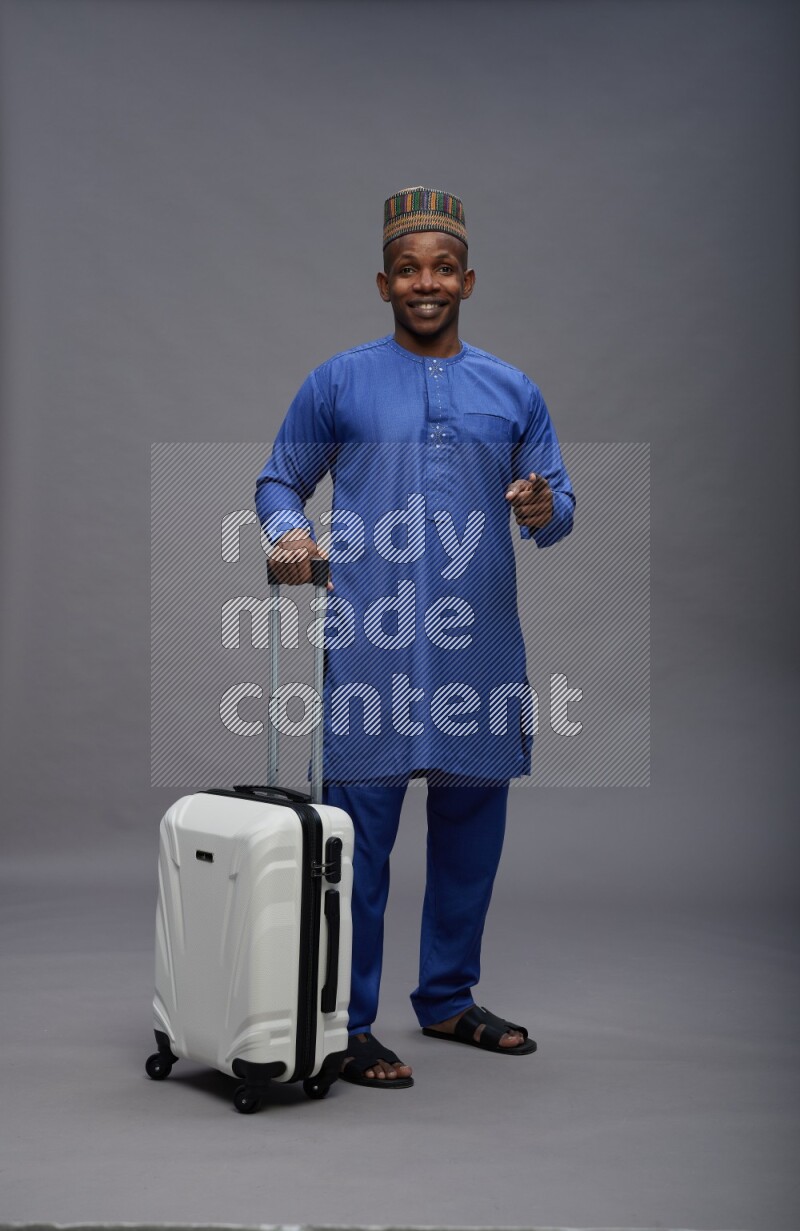 Man wearing Nigerian outfit standing holding bag on gray background