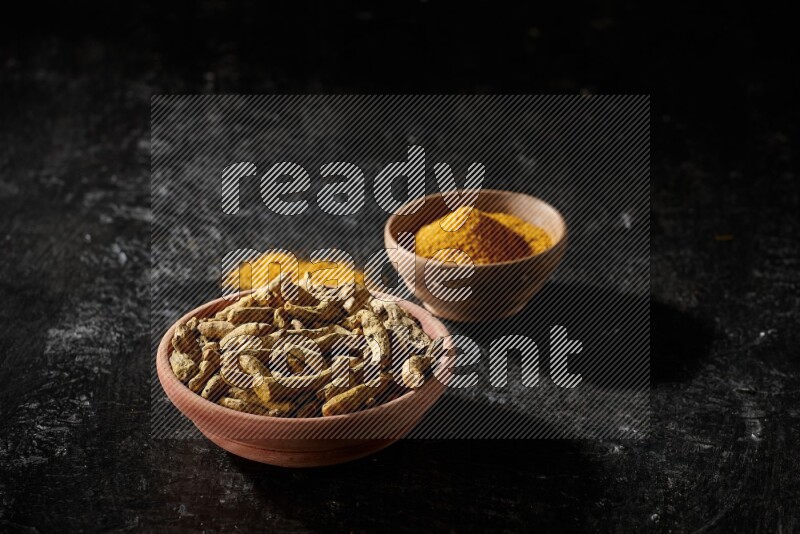 وعاءان خشبيان، أحدهما ممتلئ ببودرة الكركم والآخر بأصابع الكركم المجففة، على خلفية سوداء