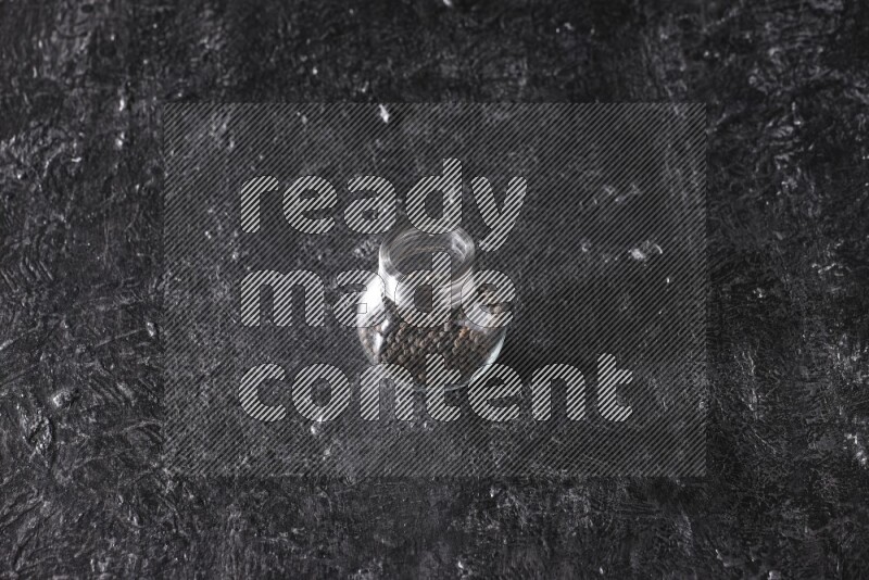 حبوب الفلفل الأسود في وعاء زجاجي علي خلفية سوداء