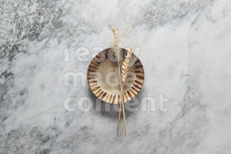 Wheat stalks on multicolored pottery plate on grey marble background