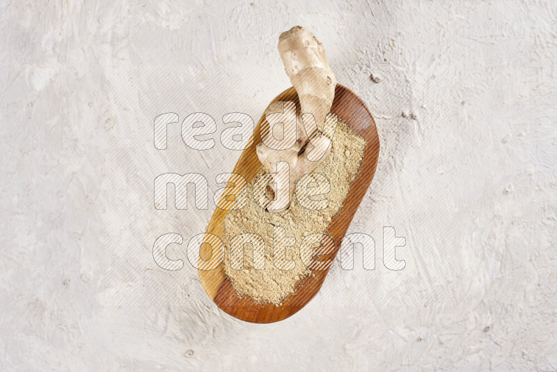 A wooden plate full of ground ginger powder with fresh root in it on white background