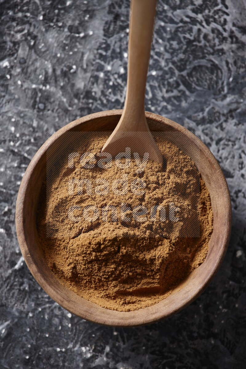 Wooden bowl full of cinnamon powder with a wooden spoon on a textured black background in different angles