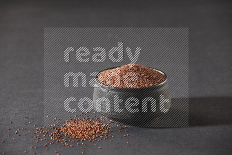 A black pottery bowl full of garden cress seeds on a black flooring