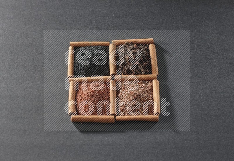 4 مربعات من عيدان القرفة ممتلئة بحبة البركة السوداء وحب الرشاد وبذور الكتان والقرنفل على أرضية سوداء