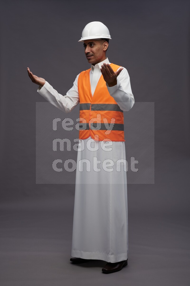 Saudi man wearing thob with engineer vest standing interacting with the camera on gray background