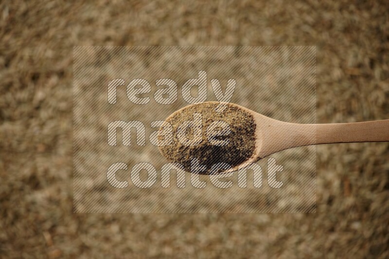 A wooden spoon full of cumin powder on a cumin seeds background