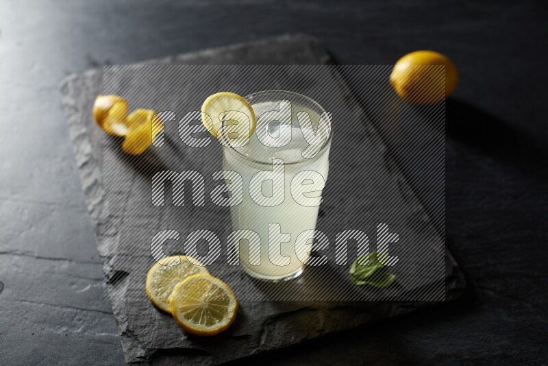 A glass of lemon juice with a lemon slice on black background