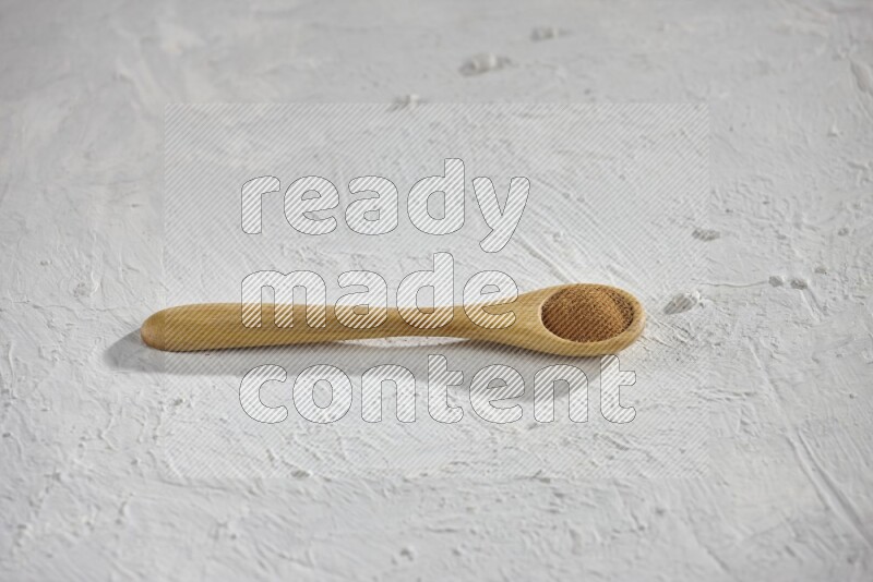 Cinnamon powder in a wooden spoon on a white background