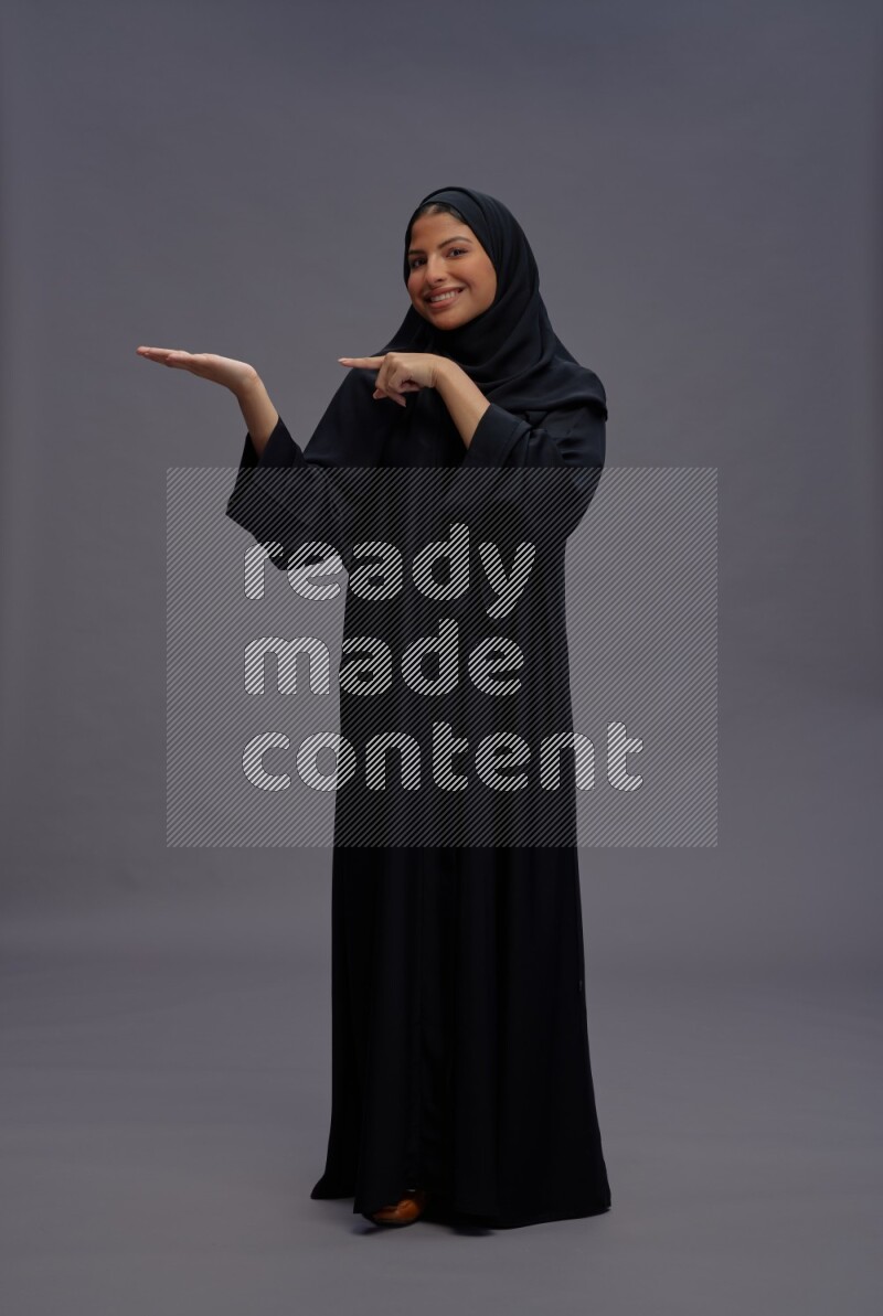 Saudi woman wearing Abaya standing interacting with the camera on gray background