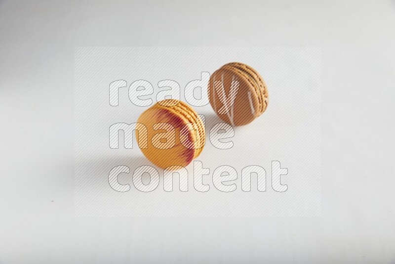 45º Shot of of two assorted Brown Irish Cream, and Orange Exotic macarons on white background
