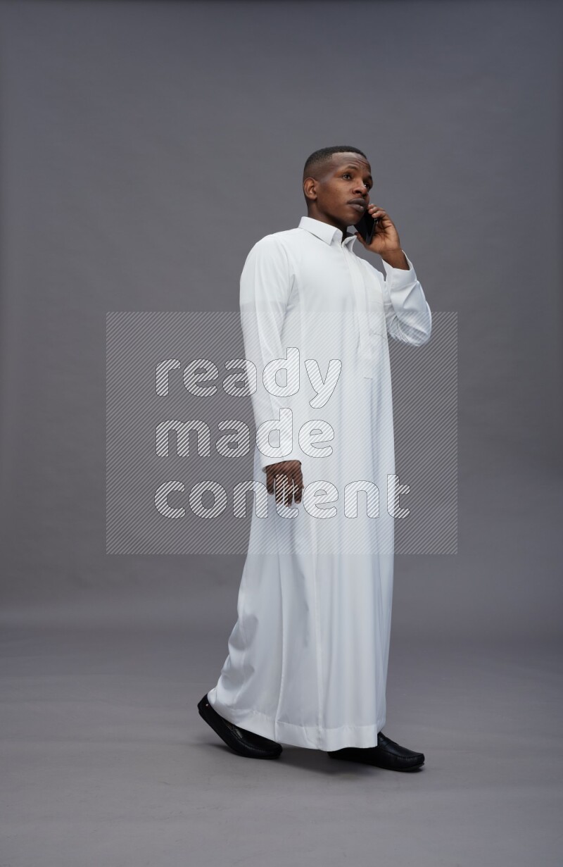 Saudi man wearing thob standing talking on phone on gray background