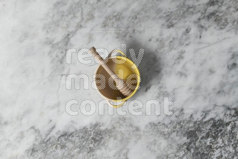 Multicolored pottery bowl with wooden honey dipper in it on grey marble background