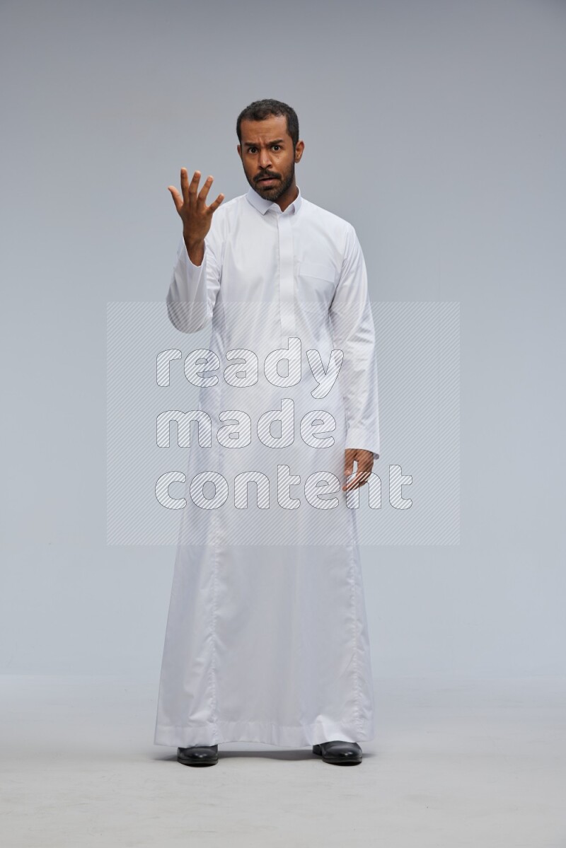 Saudi man Wearing Thob standing interacting with the camera on Gray background