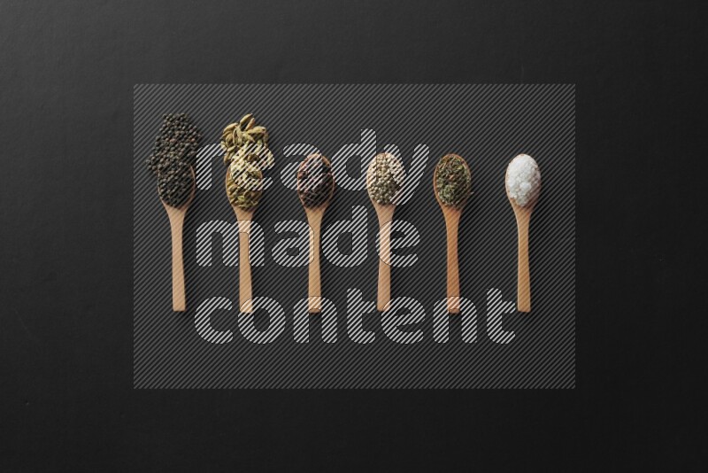 الفلفل الأبيض والقرنفل والهيل والملح والفلفل الأسود وريحان مجفف في معالق خشبية علي خلفية سوداء