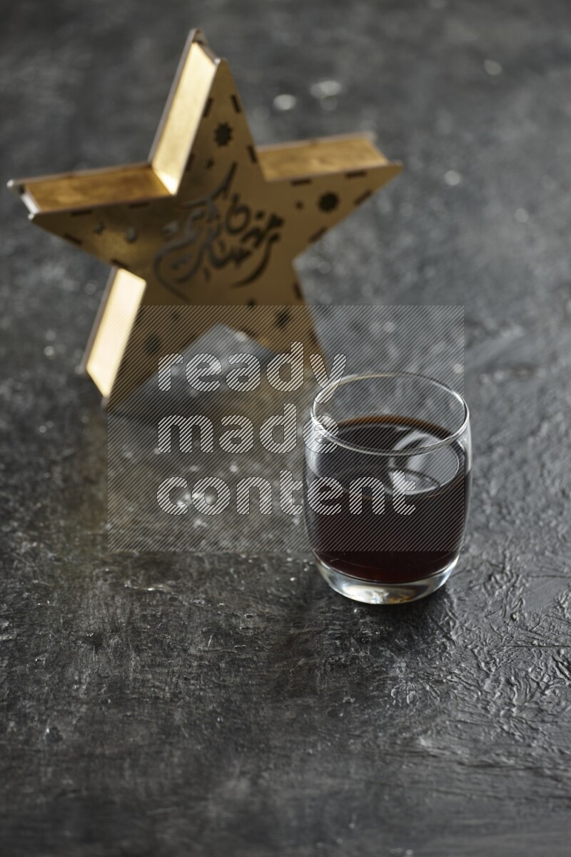 A wooden golden star lantern with different drinks, dates, nuts, prayer beads and quran on textured black background