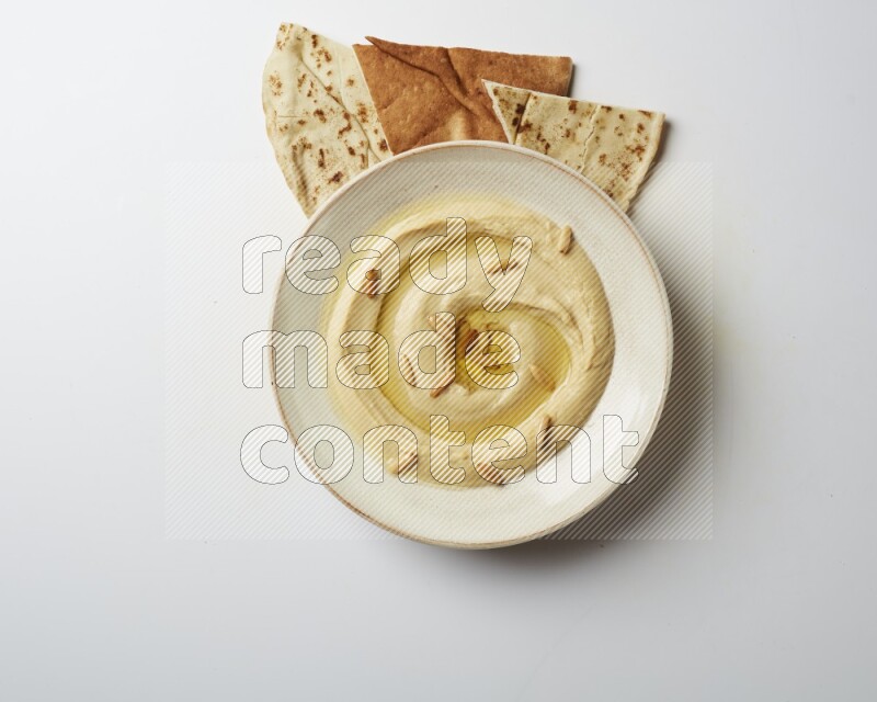 Hummus in a pottry plate garnished with pine nuts on a white background