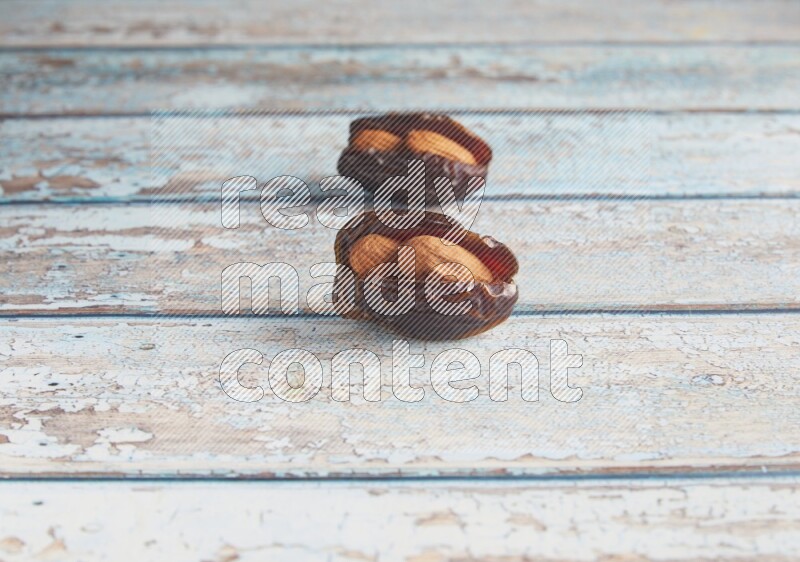 two almond stuffed madjoul dates on a light blue wooden background