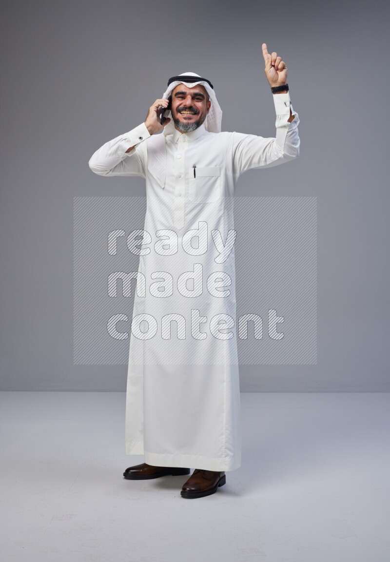 Saudi man Wearing Thob and white Shomag standing talking on phone on Gray background