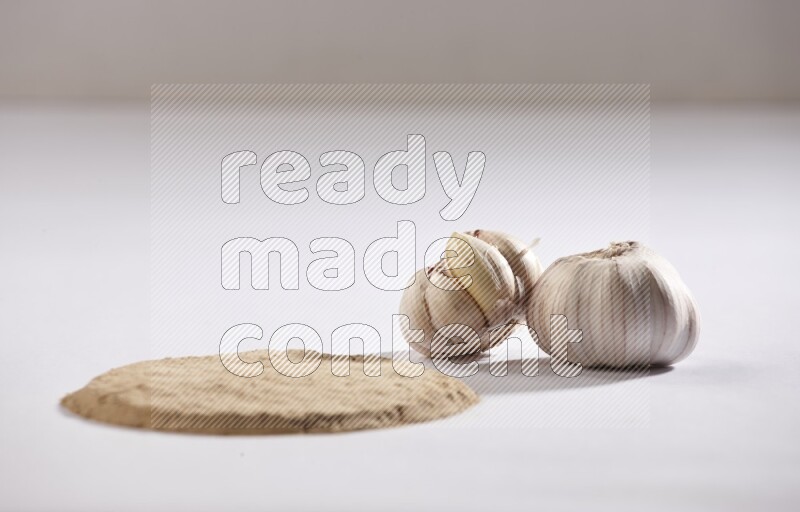 Garlic powder in a circle shape and beside it 2 garlic bulbs on a white flooring