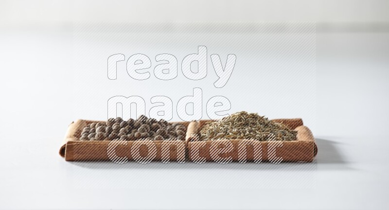 مربعان من أعواد القرفة ممتلئان ببهار الفلفل الحلو والكمون علي خلفية بيضاء