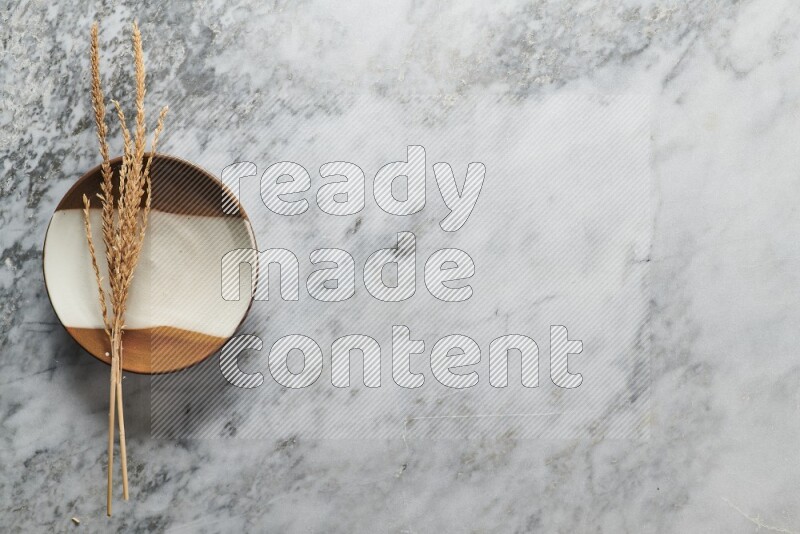 Wheat stalks on multicolored pottery plate on grey marble background