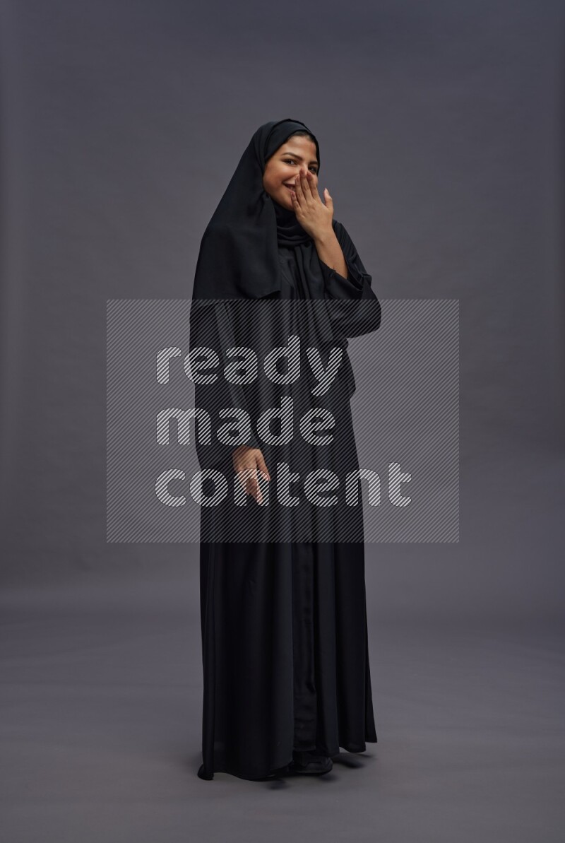 Saudi woman wearing Abaya standing interacting with the camera on gray background