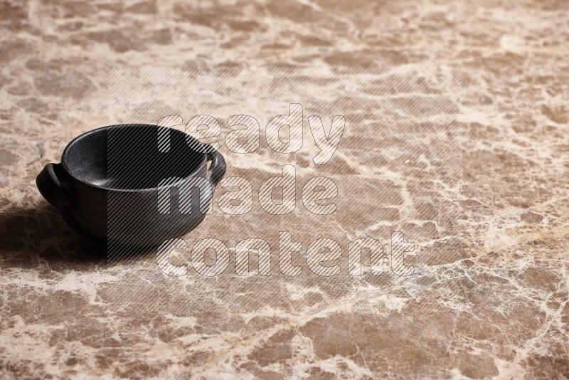 A black pottery bowl on beige marble background