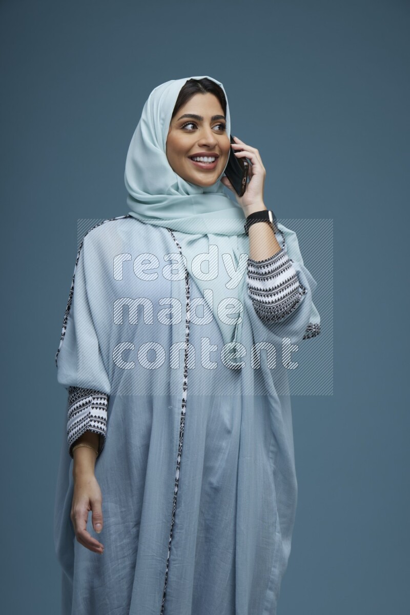 A Saudi woman having a Call in a blue background wearing blue Abaya with hijab