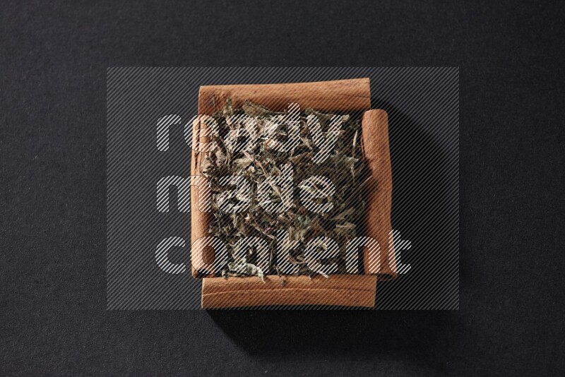 A single square of cinnamon sticks full of dried basil on black flooring