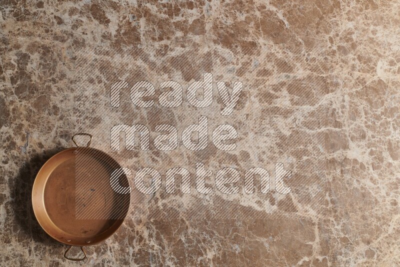 A small copper pan on beige marble background