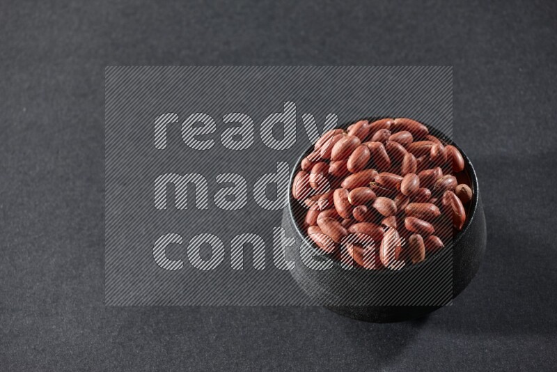 A black pottery bowl full of red skin peanuts on a black background in different angles