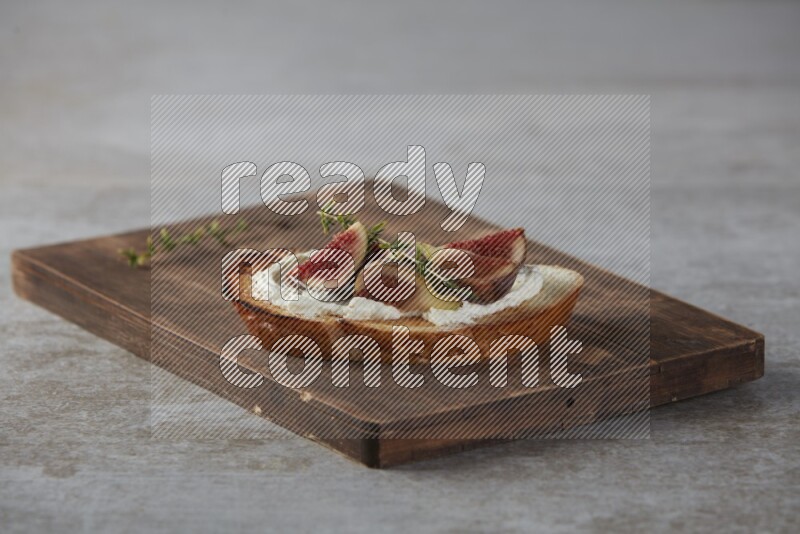 quarters of figs with cream cheese on toasted sourdough slice on a wooden board on textured grey background
