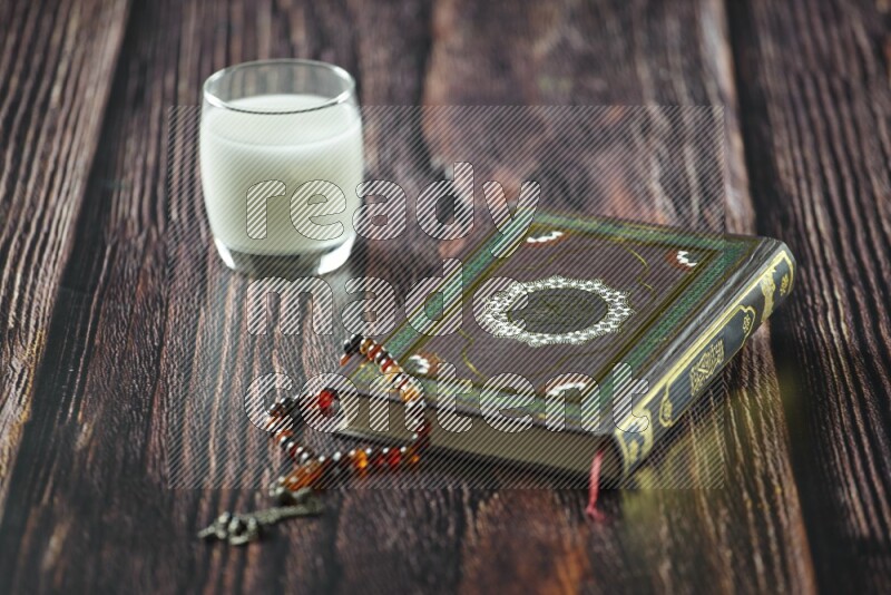 Quran with dates, prayer beads and different drinks all placed on wooden background