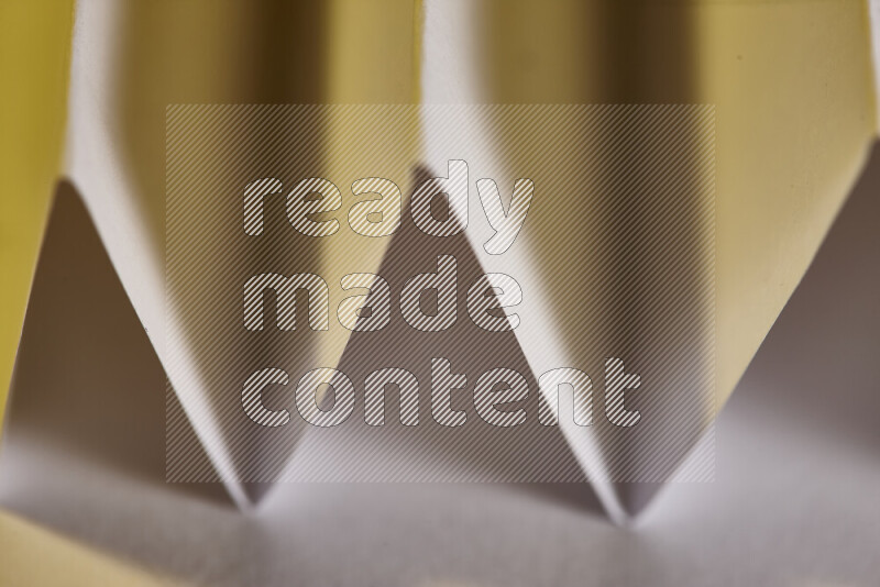 A close-up abstract image showing sharp geometric paper folds in white gradients and warm tones