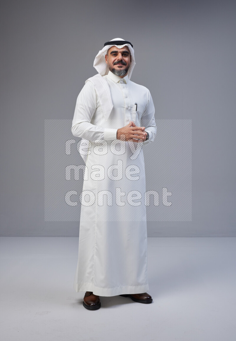 Saudi man Wearing Thob and white Shomag standing interacting with the camera on Gray background