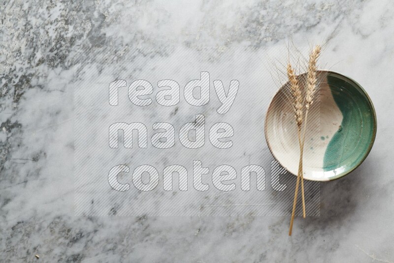 Wheat stalks on multicolored pottery plate on grey marble background