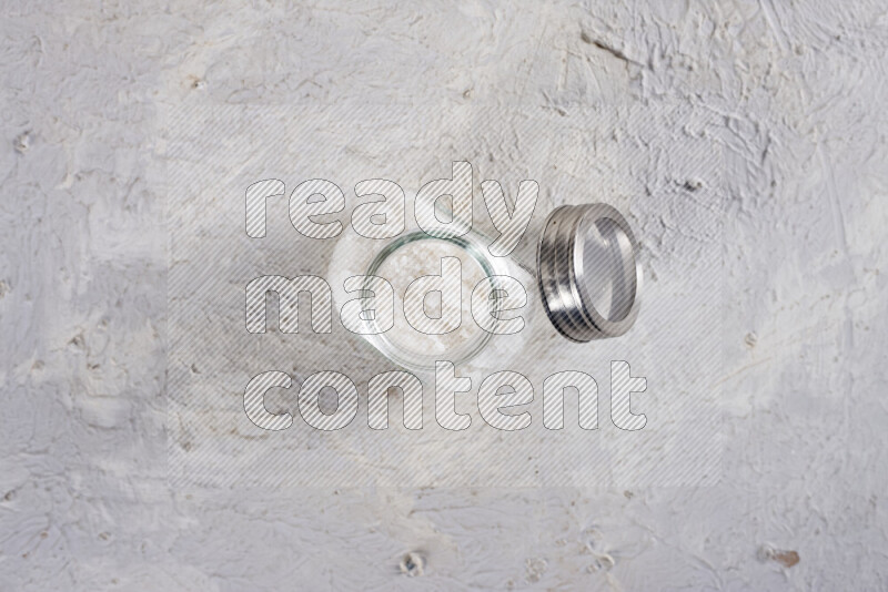 A glass jar full of coarse sea salt crystals on white background