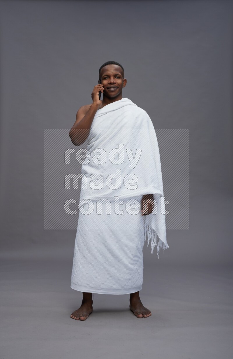 A man wearing Ehram Standing talking on phone on gray background