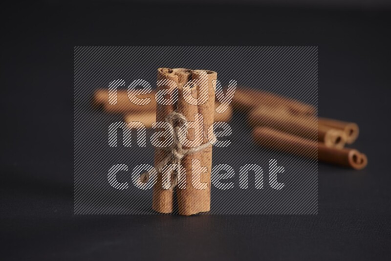 4 Cinnamon sticks stacked and bounded with more sticks in the background on black flooring
