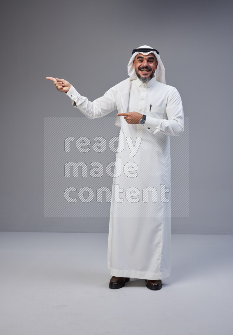 Saudi man Wearing Thob and white Shomag standing interacting with the camera on Gray background