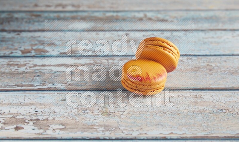 45º Shot of two orange Exotic macarons on light blue wooden background