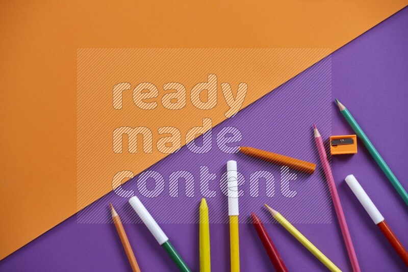 A mix of colored pencils, crayons on orange and purple background