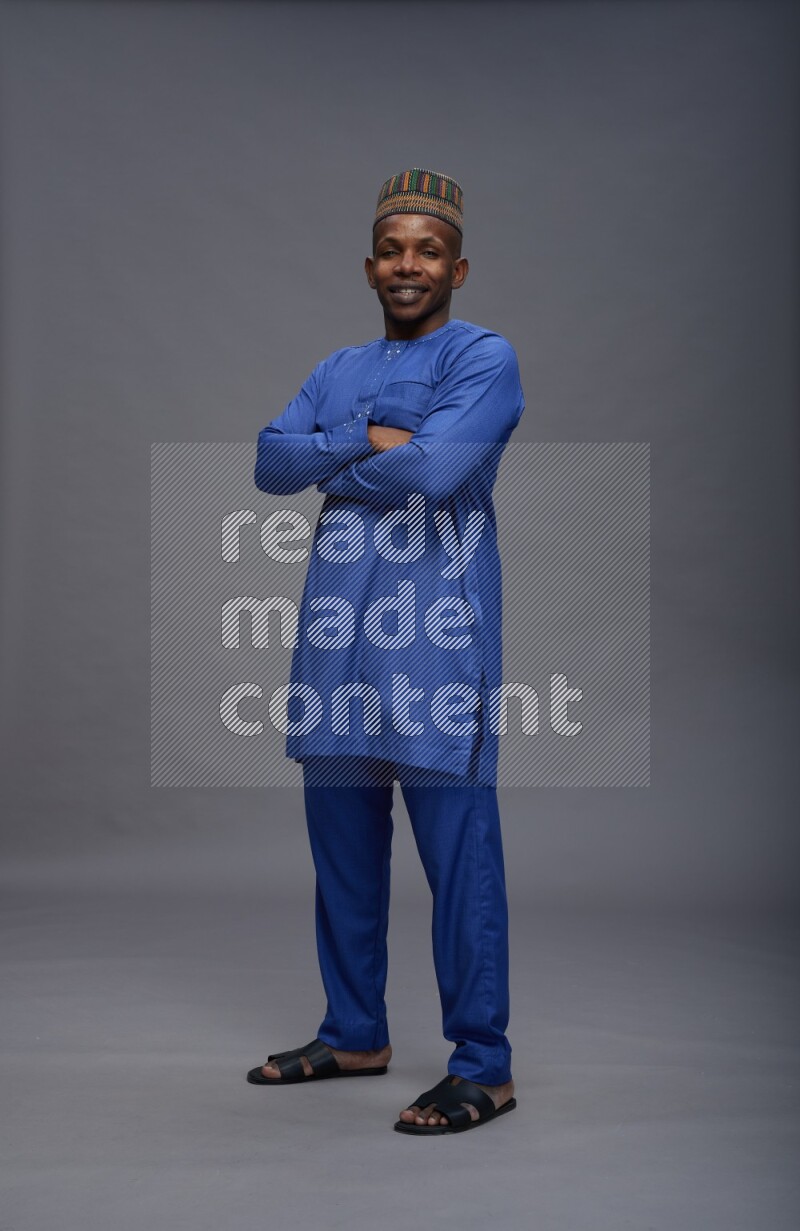 Man wearing Nigerian outfit standing with crossed arms on gray background
