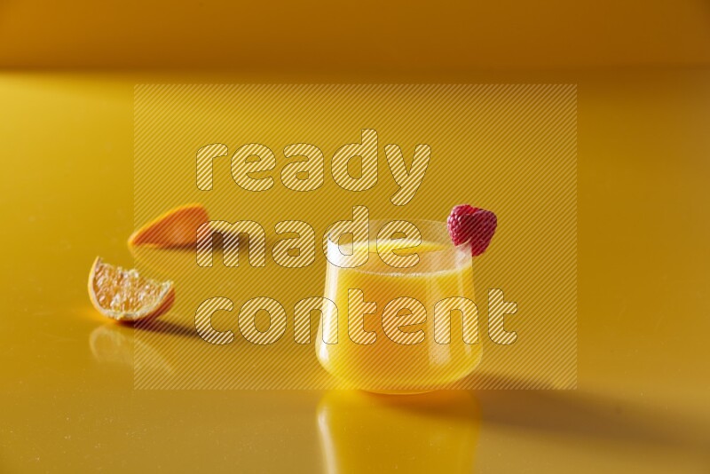 glass of orange juice with berry on yellow background
