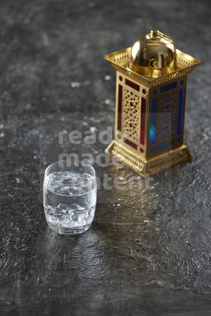 A golden lantern with different drinks, dates, nuts, prayer beads and quran on textured black background